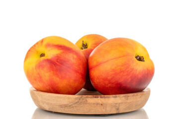 Three juicy organic nectarines on a wooden saucer, close-up, isolated on a white background.