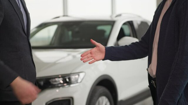 vehicle purchase, happy male buyer takes keys to a new car and shakes hands with auto dealership manager, close-up