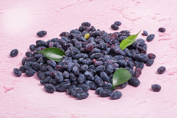 A bunch of fresh blue honeysuckle with green leaves on a pink background