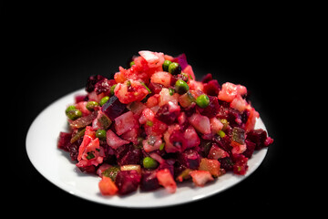 Macro closeup of traditional Russian or Ukrainian beet salad vinaigrette appetizer on table isolated black background with carrots, green peas and onions
