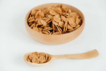 Crispy healthy dry cereal flakes in a wooden bowl with wooden spoon on white background