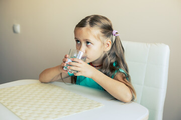 Beautiful little girl drinks clean water from a transparent glass.