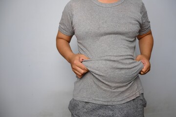 Man in gray t-shirt holding and lifting his fat flabby belly - obrazy, fototapety, plakaty