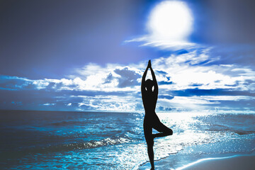 Silhouette of woman in tree pose of yoga. Sun sky and sea. Concept of calm and harmony. Blue...
