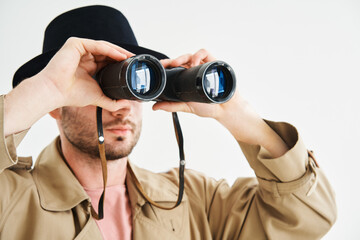 Fototapeta premium Young man wearing in coat and hat looking through binoculars over isolated white background