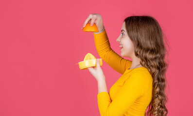 happy teen kid hold orange and juicer on pink background ith copy space