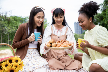 Diversity of young woman drinking beverages with baguette and pretzel on brown tray while picnic in...