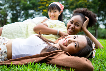 Naklejka na ściany i meble Smiling of diversity women laying on grass with bright smile in summer season at the park. Enjoy with nature and natural therapy