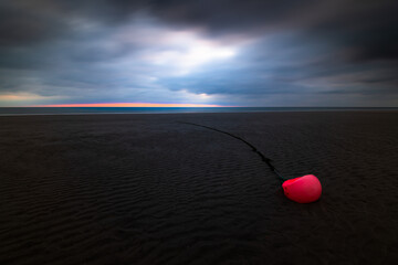 Orange buoy at the beach of Amrum island Germany during low tide with glowing dramatic sky and dark stormy clouds at sunset