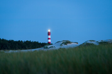 Lighted lighthouse on the dunes of Amrum island Germany with clear blue sky after sunset