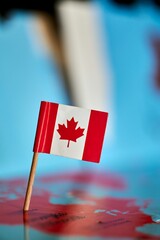 Closeup of a flag of Canada with a small stick on the map