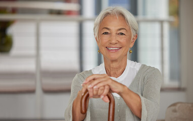 Portrait of a retired senior woman holding a wooden cane and smiling while sitting at home. Happy...