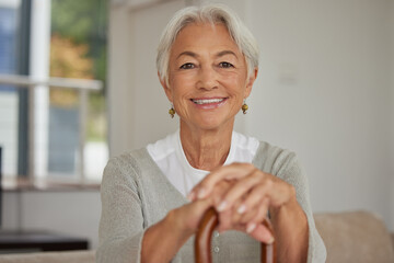 Retired senior woman relaxing at home. Happy smiling old woman holding walking cane and looking at the camera with positivity. Carefree and mature grandmother sitting on chair in nursing home