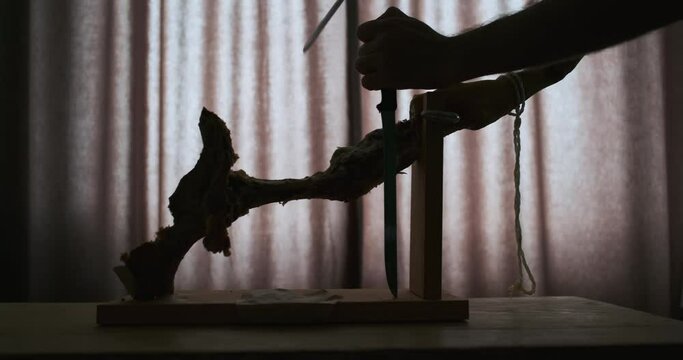 silhouette of gnawed leg of jamon on wooden stand. Hands with long knives, cutting jamon from the bone.