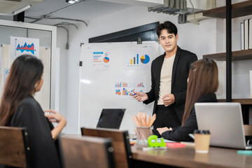 An Asian businessman is presenting his company performance report to his boss or group of male and female colleagues with confidence and professionalism.