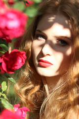 Woman with long hair posing near roses in the garden. Art portrait of a Girl on a background of roses. Girl and rose bushes. Beautiful young  Portrait of young Woman in the spring time. Rose Garden.