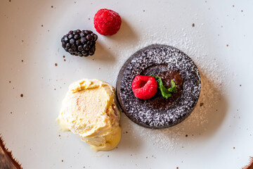 Chocolate fondant (cupcake) with raspberries, ice creme and powdered sugar placed on plate