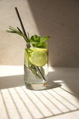 Drink in a glass with mint, rosemary, lemon and lime on a stone table with shadow. Summer drink lemonade