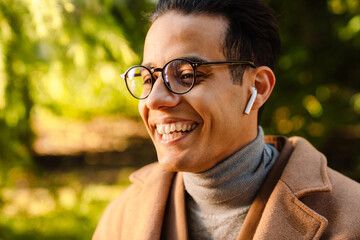 Young man wearing glasses listening music and laughing in park