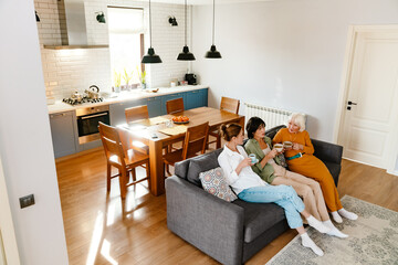 Mature three women talking and drinking tea while sitting on sofa