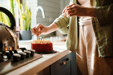 Mature woman sticking candles in birthday cake at home