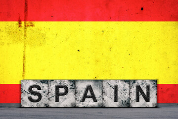 Spain, words on stone blocks, on grunge background of Spain flag, on a concrete wall. Copy space. Signs and symbols.