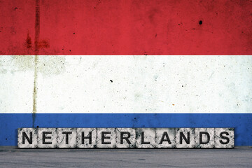 Obraz premium Netherlands, words on stone blocks, on grunge background of Netherlands flag, on a concrete wall. Copy space. Signs and symbols.