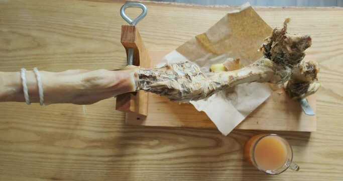 Gnawed leg of jamon on wooden stand, top view. Wooden table with cup of juice. The concept of the end of fun, the food is over