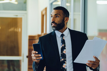 Mid adult bearded black man Entrepreneur Businessman wearing suit holding papers and smartphone...