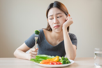 unhappy asian women is on dieting time looking at broccoli on the fork. girl do not want to eat...