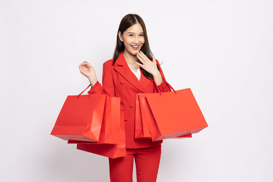 Portrait of Asian business woman in red suit holding shopping bags isolated on white background, Shopper or shopaholic concept