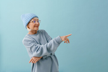 Stylish senior woman in winter hat and glasses pointing rightward