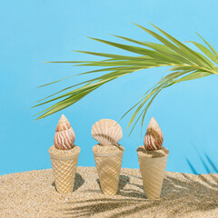 Summer beach abstract scene made of three ice cream cones with sand and sea shells and fresh palm leaf with sunshine shadow. Creative vacation concept. Surreal food idea. Vibrant blue background.
