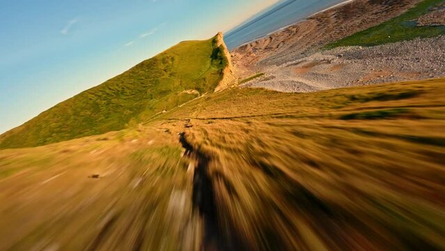 4K FPV Aerial view of monk nash beach known as the jurassic coast, stunning fast flying low across golden sandy beach with cliff side on the right.