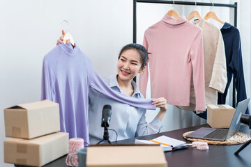 Fototapeta premium Women fashion designer stylist broadcast live streaming video to sale product and receive online order from customer and prepare packing clothes into boxes for sending delivery to client at home
