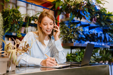 Florist girl talking on cellphone and taking notes in plant store