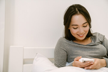 Young asian girl with phone sitting on the bed