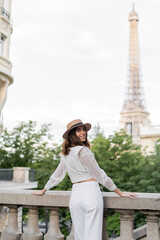 Cheerful traveler in straw hat looking t camera with Eiffel tower at background in France.