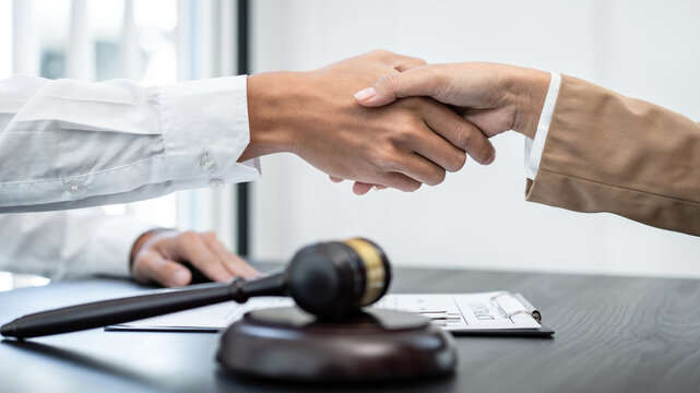 Businesswoman shaking hands with Professional male lawyer after discussing a good deal of contract in the courtroom, Concepts of law, Judge gavel with scales of justice