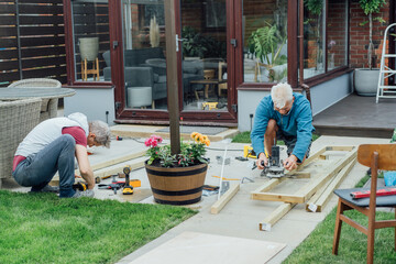 Adult son and father carpenter working together, handle wooden timbers in the garden. Patio...