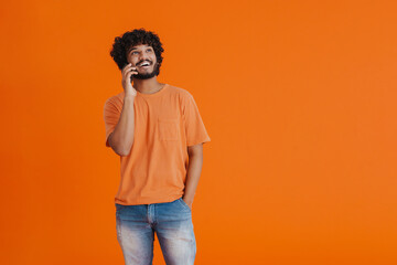 Young indian smiling man talking phone looking aside