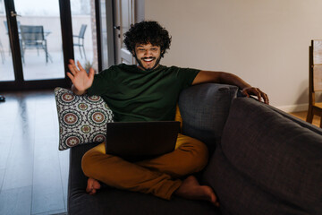 Fototapeta premium Young indian smiling handsome man holding video conference with laptop
