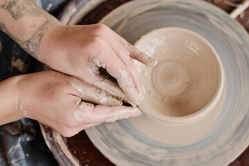 Overview of hands of young craftswoman forming shape of clay jug or pot rotating on pottery wheel while creatine earthenware