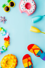 Flat lay of summer vibes concept with colorful pool party items, funny sunglasses, cocktail glasses, pineapple and donut inflatable drink holders, flip flops and flower necklace on the blue background