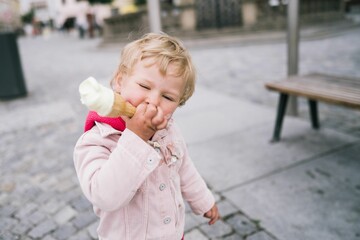 Blonde Caucasian little girl eating a melting ice cream cone outside