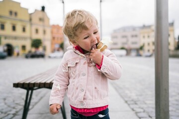 Blonde Caucasian little girl eating a melting ice cream cone outside