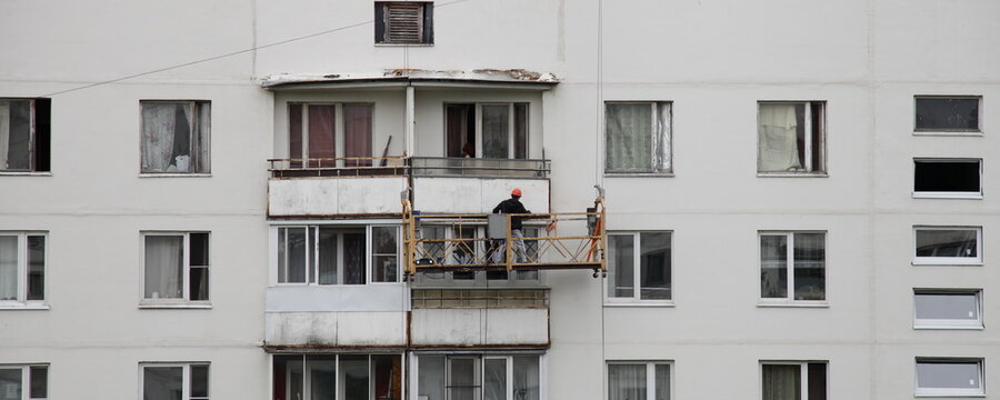 Old multi storey Russian residential house balcony wall restoration. Facade with worker on Building cradle bucket