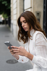 Tourist in blouse using mobile phone on urban street in Paris.