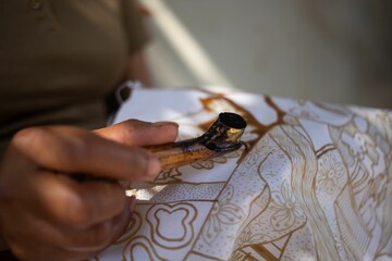 Closeup shot of an artist working on a batik fabric design in a blurred background
