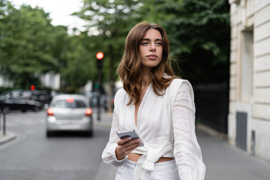 Brunette traveler in blouse holding smartphone near road in Paris.